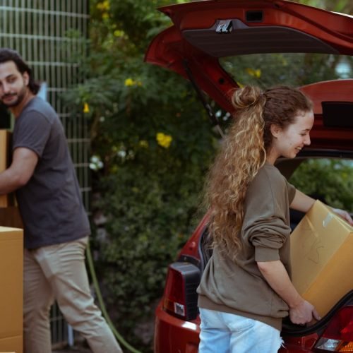 A cheerful young couple unloading boxes from a car trunk into their new home in the countryside.